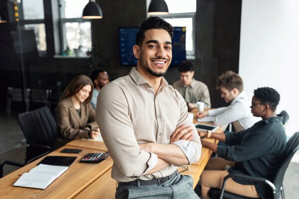 Confident smiling bearded businessman sitting leaning on desk in office