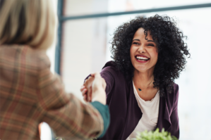 Two women shaking hands across a table.