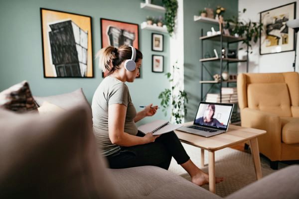 woman listening to online lecture and taking notes while she sits on a couch