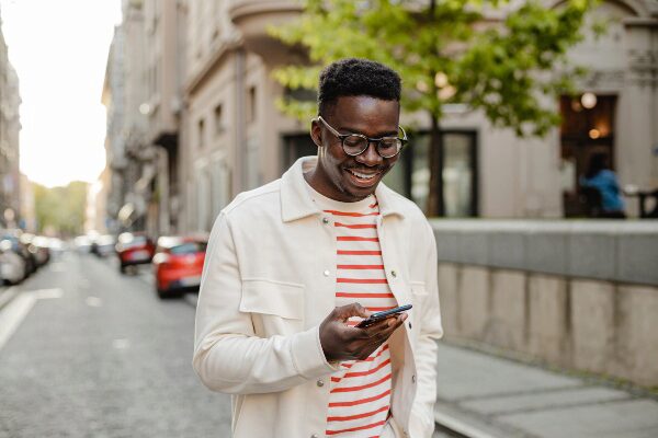 Young man smiling at his cellphone while walking down a urban street