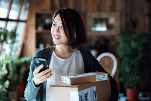 Happy young woman with cell phone holding shipping packages