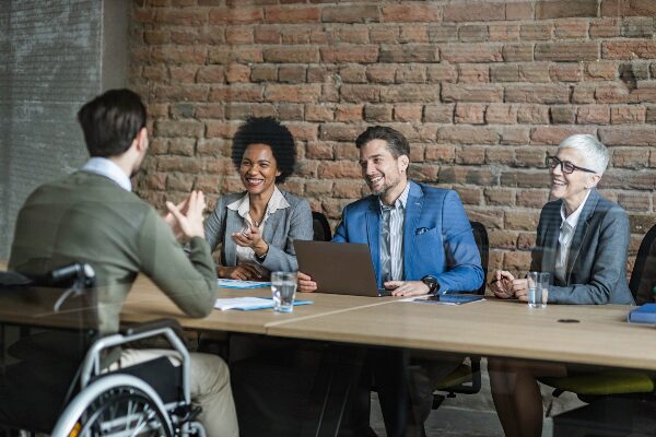 Man in a wheelchair being interviewed by three smiling people