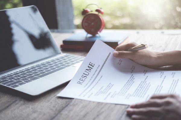 person reviewing resume on desk with laptop computer and clock