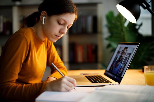 College student taking notes while listening to online lecture